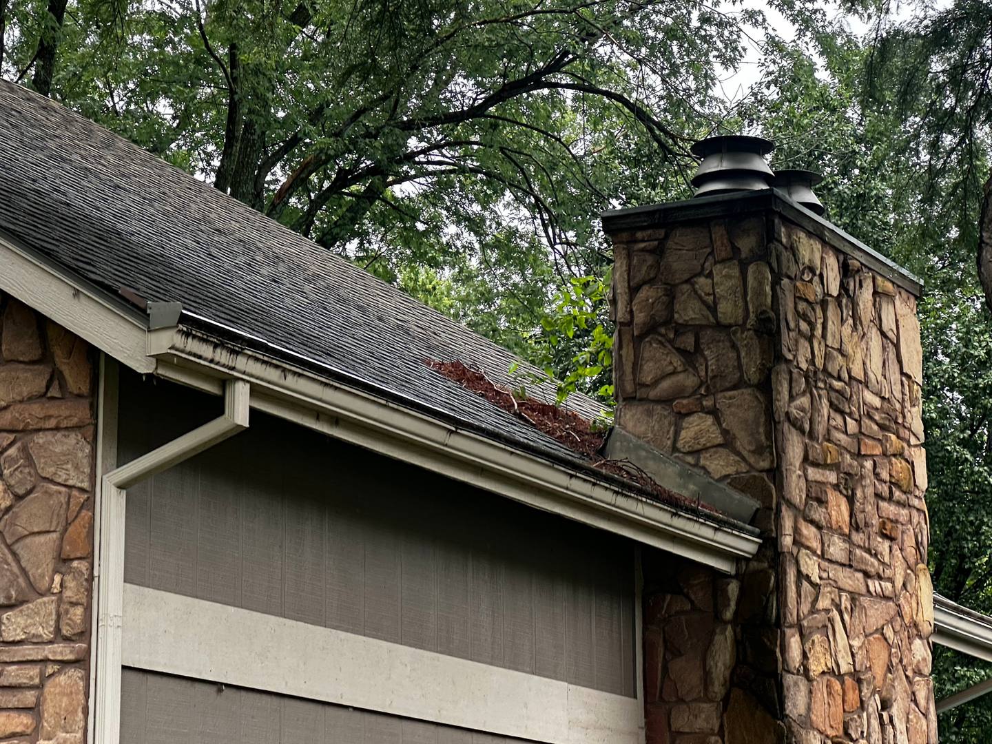 Gutter full of debris by a stone chimney before cleaning, Derby, KS
