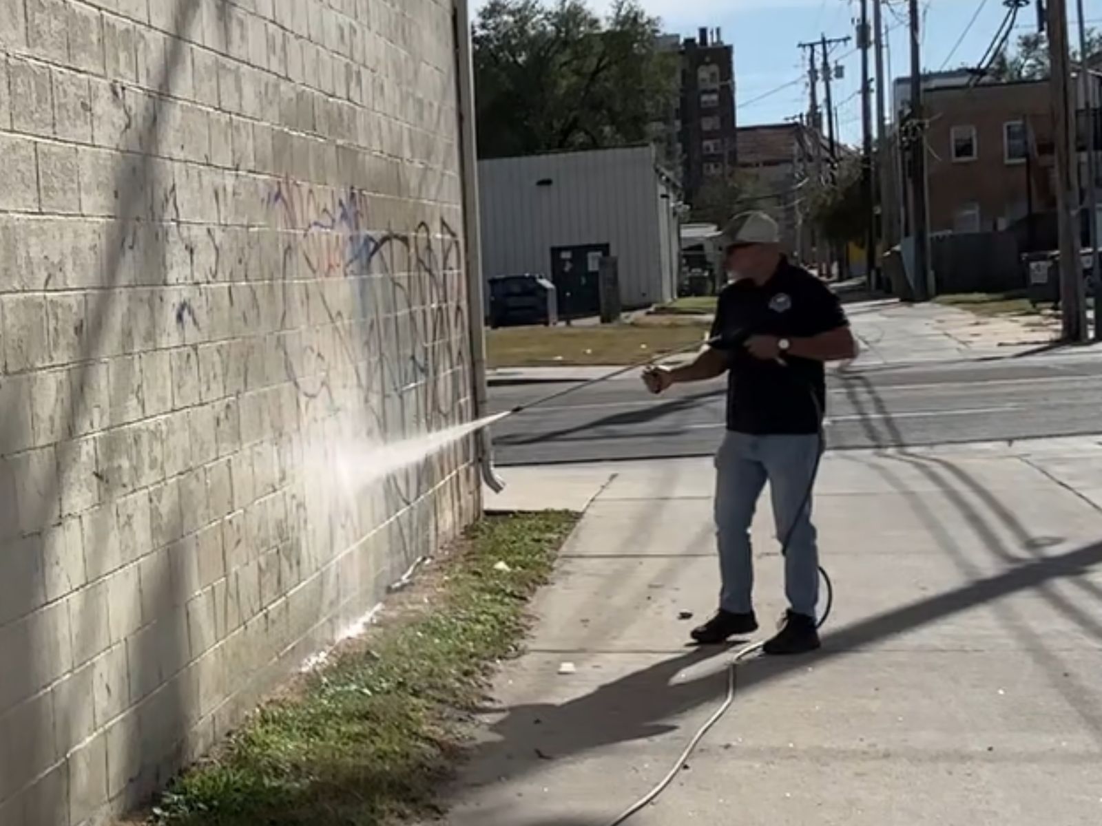 Pressure washing graffiti off a block wall in an alley