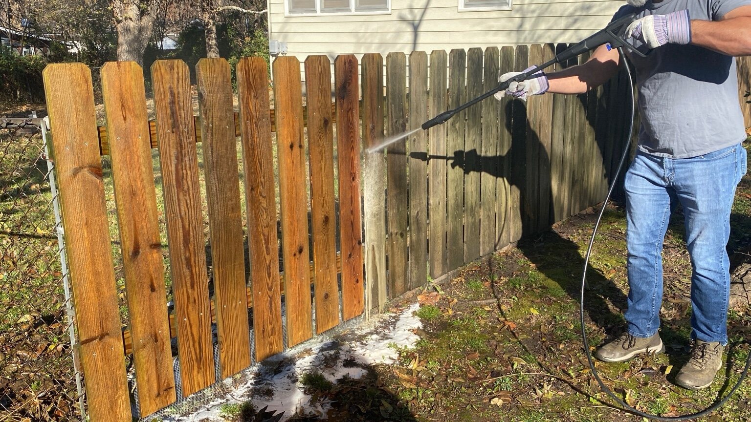 Wood fence being pressure washed with the clean section visible