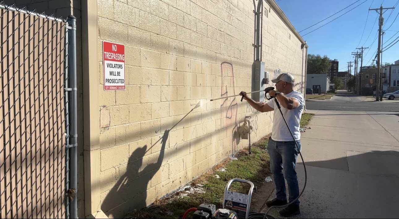 Buffalo Pressure Washing technician removing graffiti from a concrete block wall